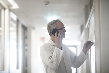Male meteorologist reading charts and talking on smartphone in weather station laboratory
