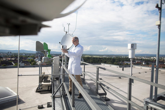 Male meteorologist updating meteorological equipment measurements at rooftop weather station