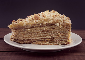 Layered cake slice with nut on plate, on wooden table, dark back