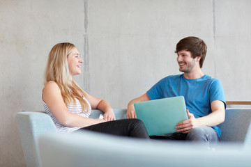 Young male and female students sitting on study space sofa with laptop at higher education college