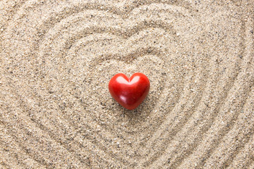 Red heart shaped stone on sand surface forming heart waves