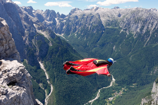 Wingsuit BASE jumper flying along cliff side and down the valley, Italian Alps, Alleghe, Belluno, Italy