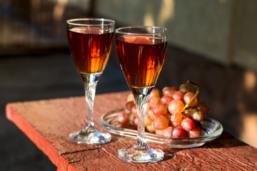 Two glasses of homemade rose wine and grapes on table at garden