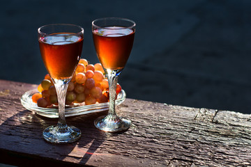 Two glasses of homemade rose wine and grapes on table at garden