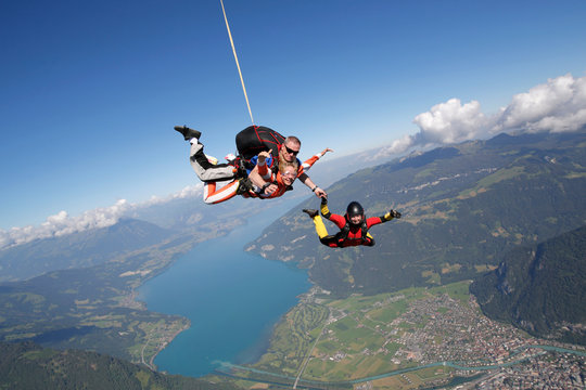 Smiling tandem sky divers holding hand with free faller, Interlaken, Berne, Switzerland