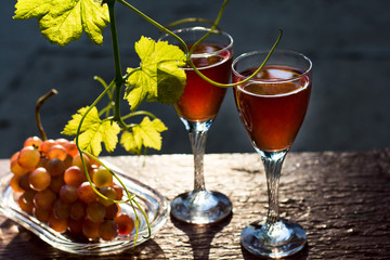 Two glasses of homemade rose wine and grapes on table at garden