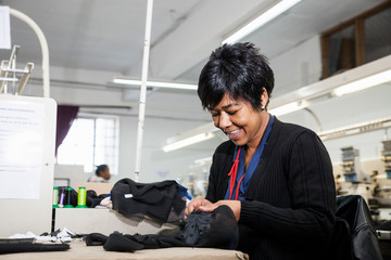 Female factory worker removing stitches from black cloth from speed stitching programmed embroidery machine in clothing factory