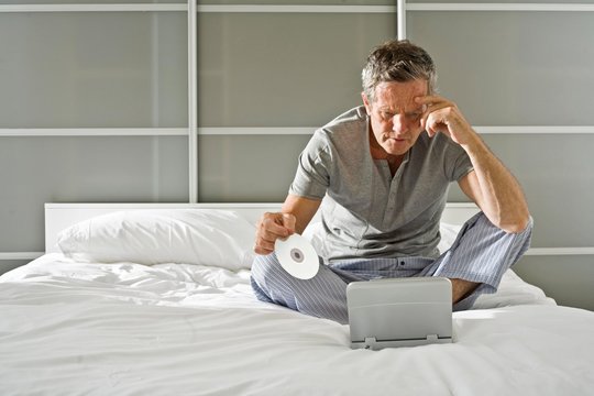 Senior man sitting up holding CD and staring at laptop