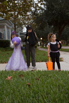Boy and sisters trick or treating looking in bags on sidewalk