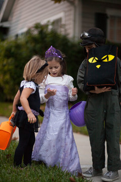 Boy and sisters trick or treating looking at treats on sidewalk