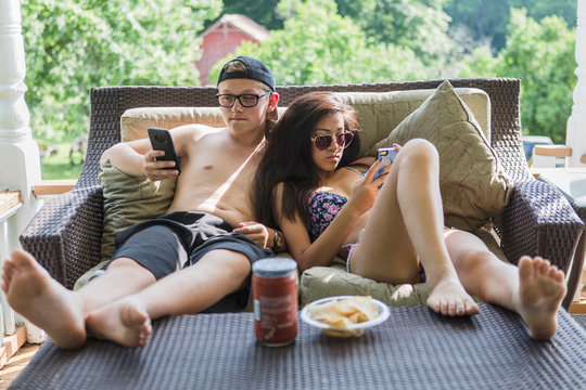 Teen couple sitting on porch with smartphones