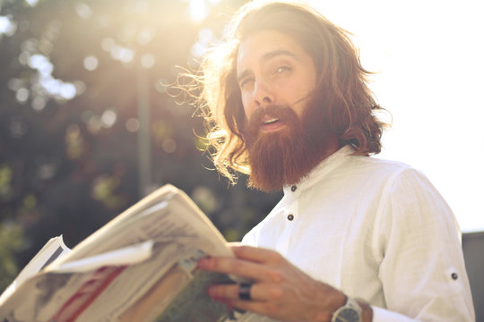 Young man with long hair and beard reading the newspaper