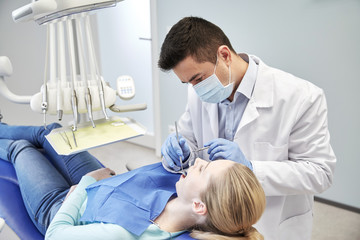 Fototapeta premium male dentist in mask checking female patient teeth