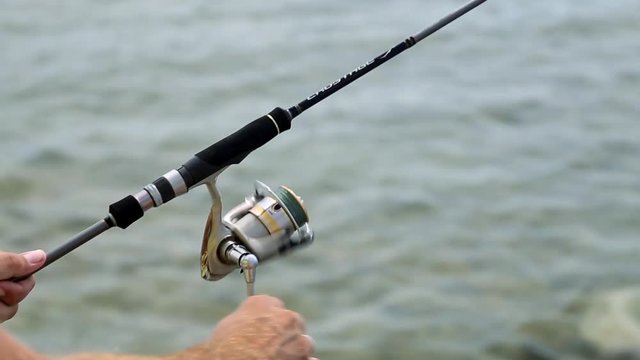 Spinning Reel. Sea fishing. A man fishing on the coast. Fisherman with spinning. The hand rotates the reel spinning.