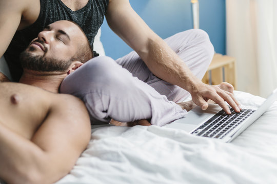 Gay couple lying in bed, using laptop