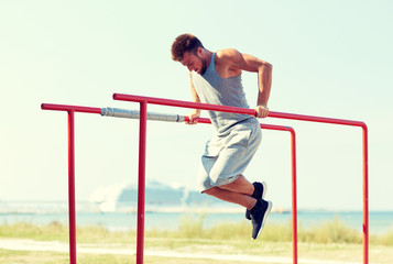 young man exercising on parallel bars outdoors - obrazy, fototapety, plakaty