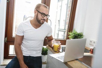 Gay man drinking orange juice while reading emails