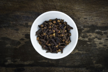 Heap of dried cloves in bowl on wooden background