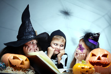 Three little children sitting together with a book among pumpkins