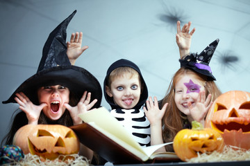 Portrait of three little children in Halloween fancy dresses making faces among pumpkins