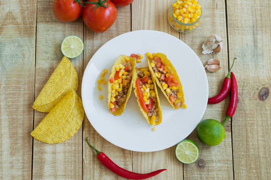 Fresh mexican tacos with tomato, corn and chicken meat and ingredients on wooden background