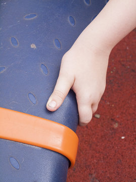 Close up of a the hand of a ten year old boy, ready to push while playing on on a piece of modern plastic playground equipment. The floor beneath is a rubber based safety surface.
