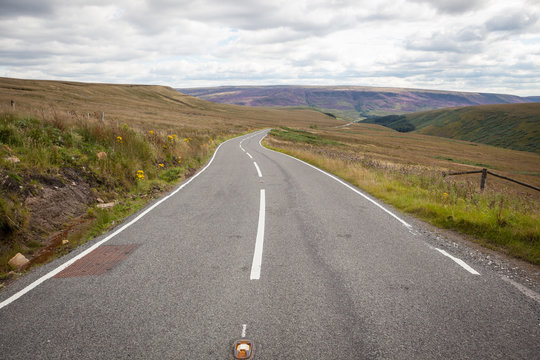 A Centered Road Without Cars Rolling Into The Horizon With Moorland On Either Side.