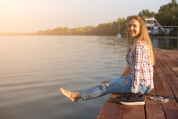 Fototapeta premium Beautiful young girl resting on a pier near the water at dawn