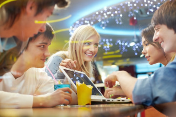 Four students sitting in cafe and discussing something on laptop