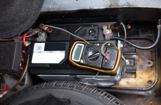 Mechanic checking a car battery level with  voltmeter