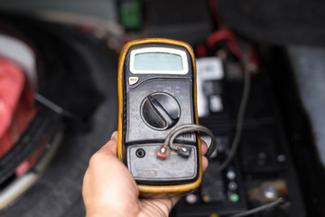 Mechanic checking a car battery level with  voltmeter