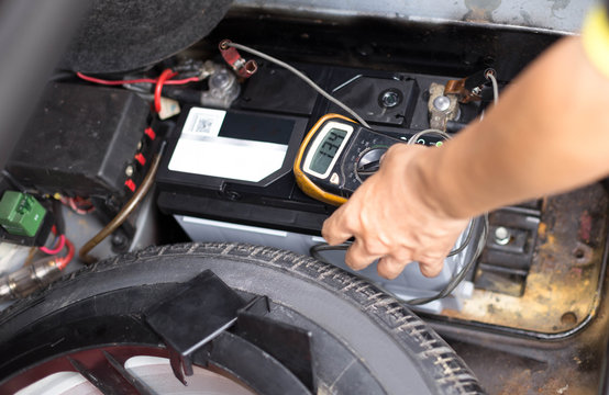 Mechanic checking a car battery level with  voltmeter