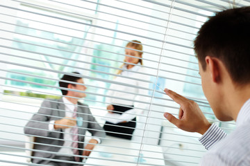 Businessman looking through blinds at his colleagues