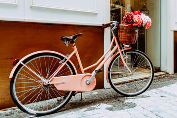 Fototapeta na wymiar Vintage Pink Bicycle With A Decorative Basket Of Flowers Parking