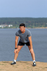 Male runner doing stretching exercise, preparing for morning workout in the park