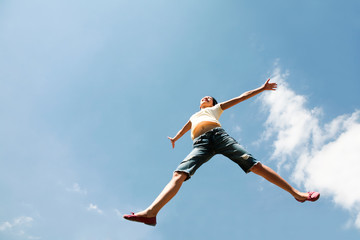 View from below of leaping happy girl on the background of blue sky
