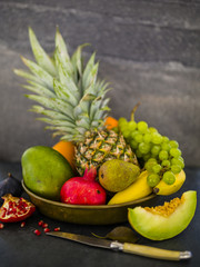 Fresh and ripe tropical fruits in old plate on dark stone background. Still life.
