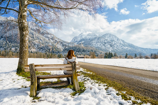 Back view of woman sitting on bench against of winter mountains