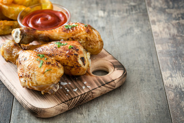 Roast chicken drumsticks with chips on wooden background
