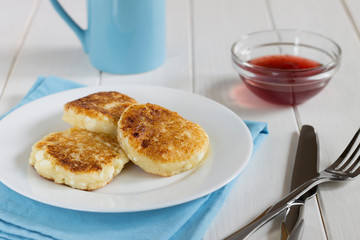 Cottage cheese pancakes with cranberry sauce on white wooden tab