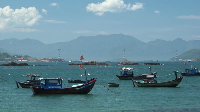 Few fishing boats are shaking on water at the local vietnamese river. Summer sunny windy day. Mountains behind.