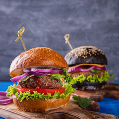 Beef burger with white and black bun,with lettuce and mayonnaise and ketchup served on pieces of brown paper on a rustic wooden the Board.selective focus