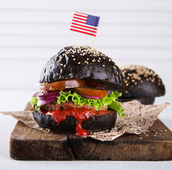 Beef burger with a black bun; with lettuce and mayonnaise  served on pieces of brown paper  of counter; on a white wooden background.patriotic 4th of july themed burgers at picnic