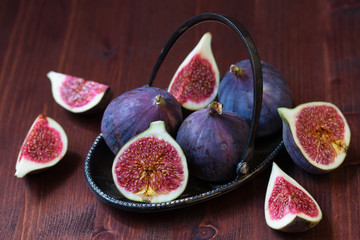 Whole and sliced figs on the dark wooden background. Selective focus.