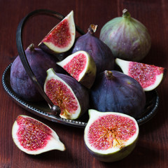 Whole and sliced figs on the dark wooden background. Selective focus.