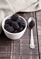 Fototapeta na wymiar Blackberry in white bowl and spoon on grunge wooden board