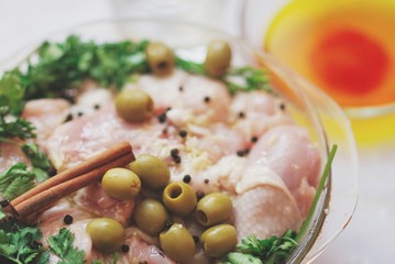 Raw chicken legs, parsley, cinnamon and spices in glass dish on white table, close up.