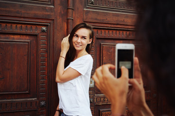 A beautiful girl is smilimg at camera of a mobile phone while standing beside the massive wooden...