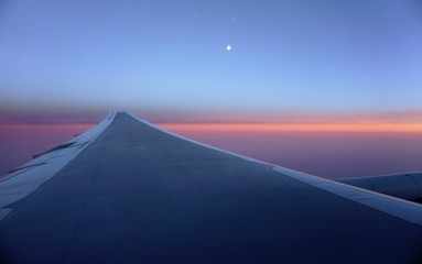 Fototapeta na wymiar A pink and blue sky with the moon over an airplane wing