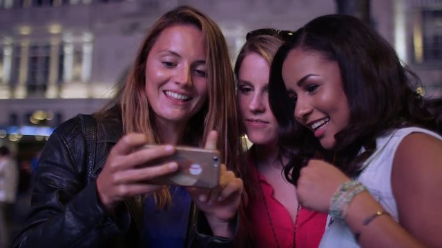 Female friends pull silly faces during a selfie in the city at night, in slow motion